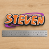 Personalized Naruto-inspired STEVEN nameplate beside a dual-scale ruler showing approximately 23 cm (9 in) width
